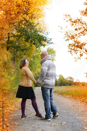 middle-aged man in a gray sweater and a woman in a yellow stand, embracing, in an autumn park against the background of trees, the concept of a healthy lifestyle, love, happiness at any age
