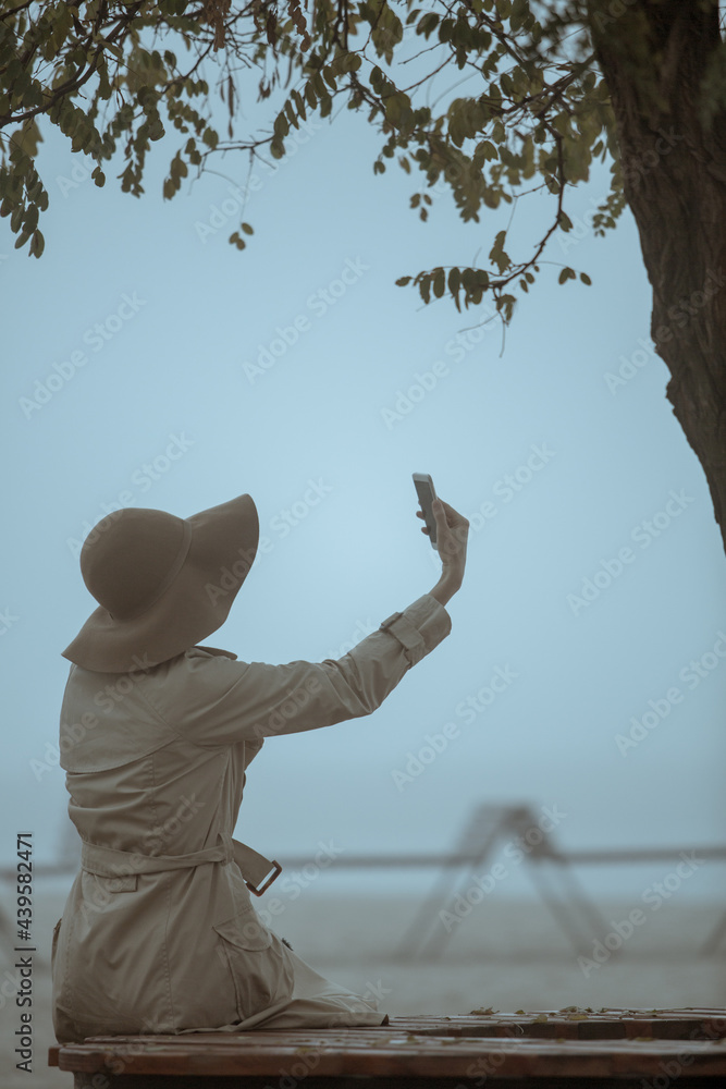 Fototapeta premium Rear view of young woman woman wearing hat a holding smart phone