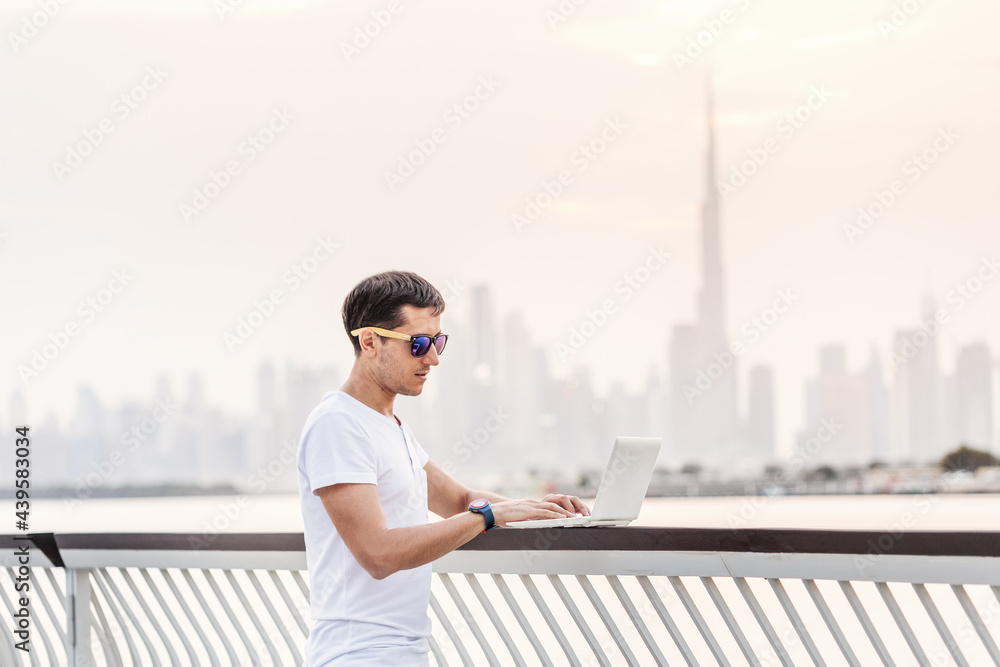Happy man freelance programmer and junior developer writes code and thinks about a project in the paradise resort city of Dubai against the backdrop of the famous Burj Khalifa skyscraper Happy man freelance programmer and junior developer writes code and thinks about a project in the paradise resort city of Dubai against the backdrop of the famous Burj Khalifa skyscraper