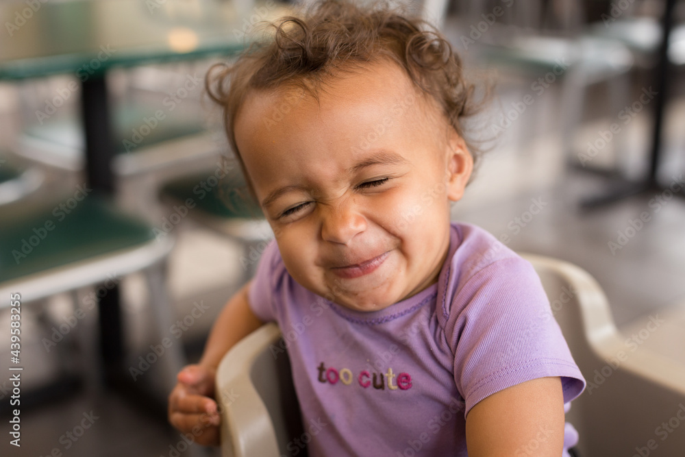 Grinning toddler in high chair squeezes eyes shut Grinning toddler in high chair squeezes eyes shut