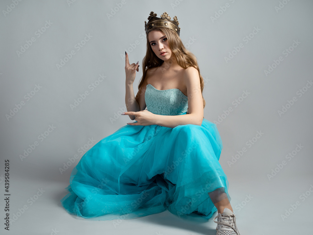 Fototapeta premium Cool princess in a lush blue dress and crown makes a rocker hand gesture,