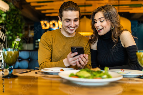 Couple in restaurant eating lunch and looking on smartphone