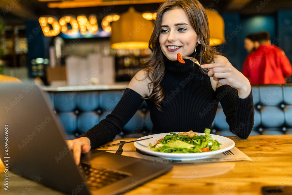 Young pretty woman sitting with a laptop in a cafe and eating breakfast