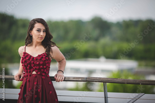 Attractive Caucasian female wearing an elegant long burgundy dress posing on the bridge photo