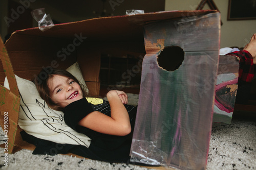 little girl lays down inside cardboard box fort photo