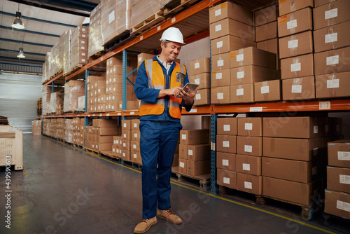 Cheerful male warehouse supervisor standing in warehouse using smart tablet