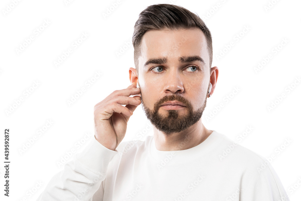 Handsome bearded man in white clothes using wireless earbuds on white background Handsome bearded man in white clothes using wireless earbuds on white background