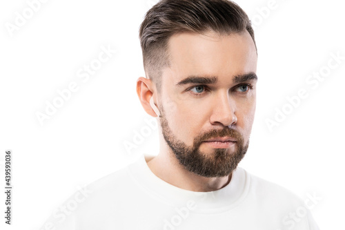 Handsome bearded man in white clothes using wireless earbuds on white background