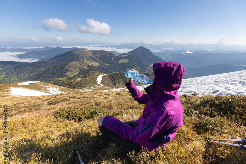 Woman hiker enjoying high peak view on mountains in summer. She is drinking water. Pip Ivan peak. Marmarosy ridge, Carpathian, Ukraine