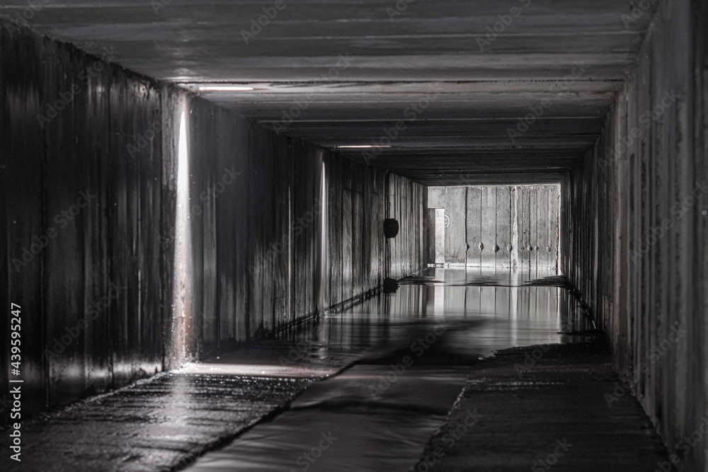 Rectangular concrete tunnel of a drainage collector with openings for rain receivers through which light shines.