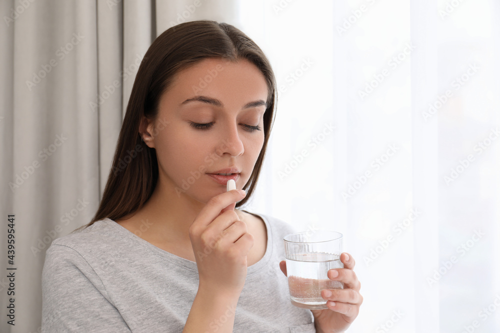 Young woman with glass of water taking pill at home Young woman with glass of water taking pill at home