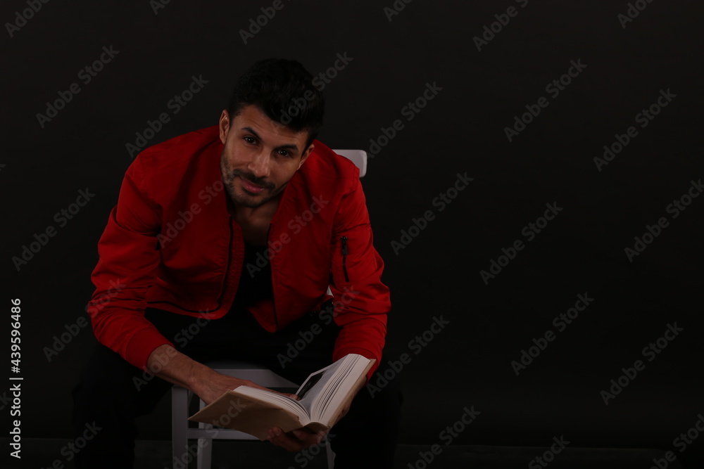A man in red jacket with a book sitting on a chair A man in red jacket with a book sitting on a chair