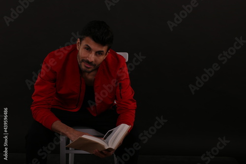 A man in red jacket with a book sitting on a chair