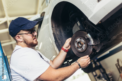 Professional near the car hanging on the lift at the service station make a diagnostics, repair the brakes