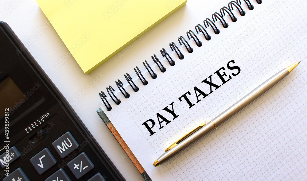 Notepad with text PAY TAXES, next to it lies a calculator. Business concept. Notepad with text PAY TAXES, next to it lies a calculator. Business concept.
