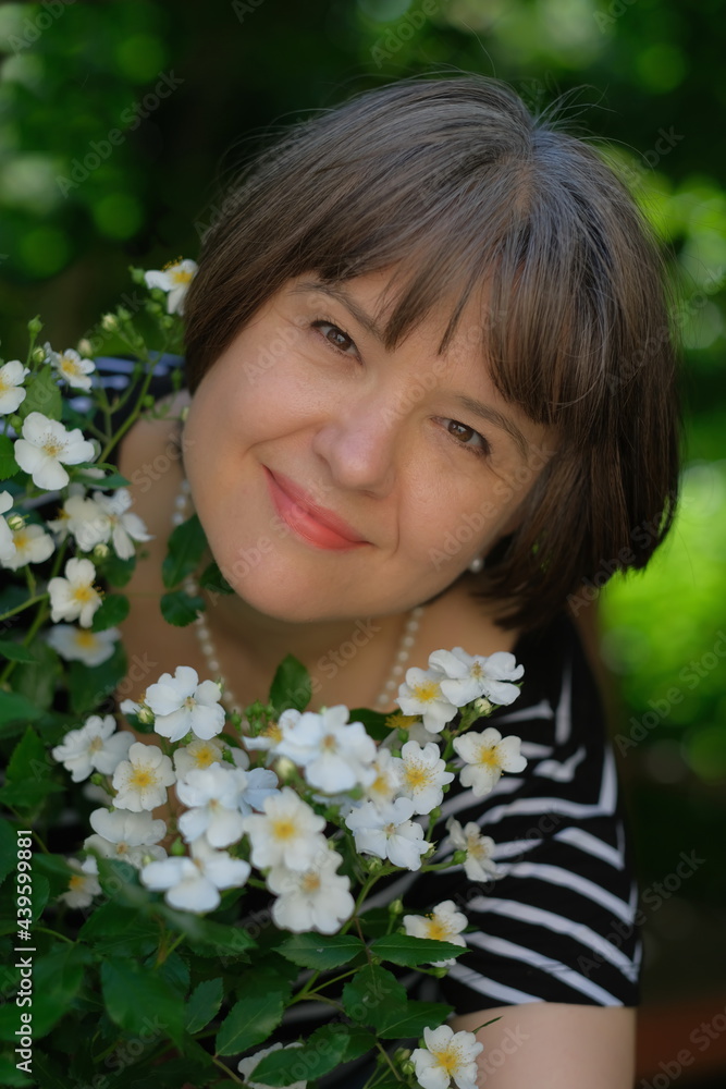 Der Kopf einer dunkelhaarige Frau mit weißer Perlenkette schaut durch kleine weiße Rosen glücklich in die Kamera. Der Kopf einer dunkelhaarige Frau mit weißer Perlenkette schaut durch kleine weiße Rosen glücklich in die Kamera.