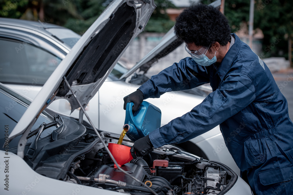 Car mechanic open car hood repairs system checking oil motor level for refill and clean in car garage service .he wearing face mask to protect from virus and pollution. Car mechanic open car hood repairs system checking oil motor level for refill and clean in car garage service .he wearing face mask to protect from virus and pollution.