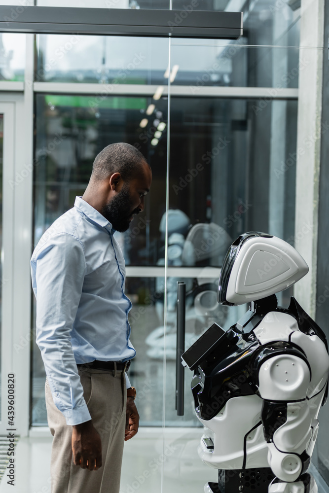 african american engineer looking at humanoid robot in office