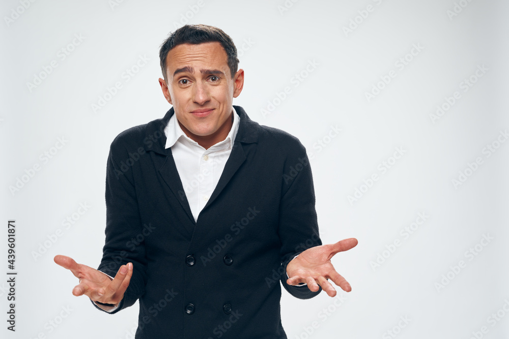 a man in a shirt and a sweater gestures with his hands on a light background a puzzled look a man in a shirt and a sweater gestures with his hands on a light background a puzzled look