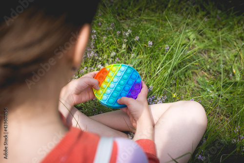 A little cute girl is sitting on the grass with a pop it - antistress toy.