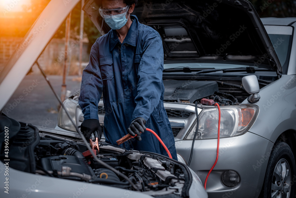 car mechanic posing to show car charger cable with battery by open hood car to check he wearing face mask to protect virus and pollution car mechanic posing to show car charger cable with battery by open hood car to check he wearing face mask to protect virus and pollution