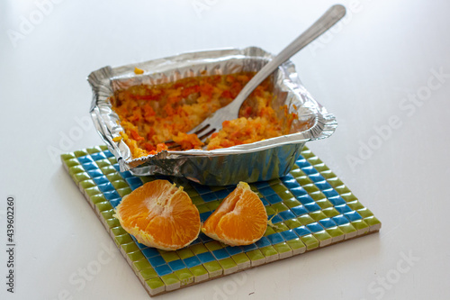 Carrot rice porridge in foil packaging and half of tangerine on a heat trivet.