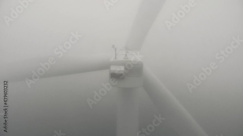 Contemporary wind machine with rotating propeller and blinking light indicator in dense mist close aerial view zoom out photo