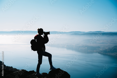 Silhouette of photographer standing on cliff edge