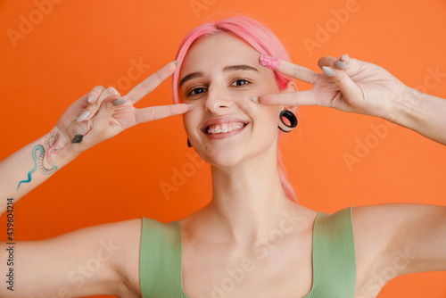 Young white woman with pink hair smiling and showing peace sign
