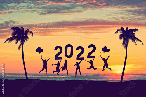 Silhouette friends jumping and holding number 2022 on sunset sky abstract background at tropical beach. Happy new year and holiday celebration concept.