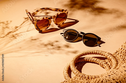 2 pairs of women sunglasses and a bag on a soft orange background and strong shadows of flowers