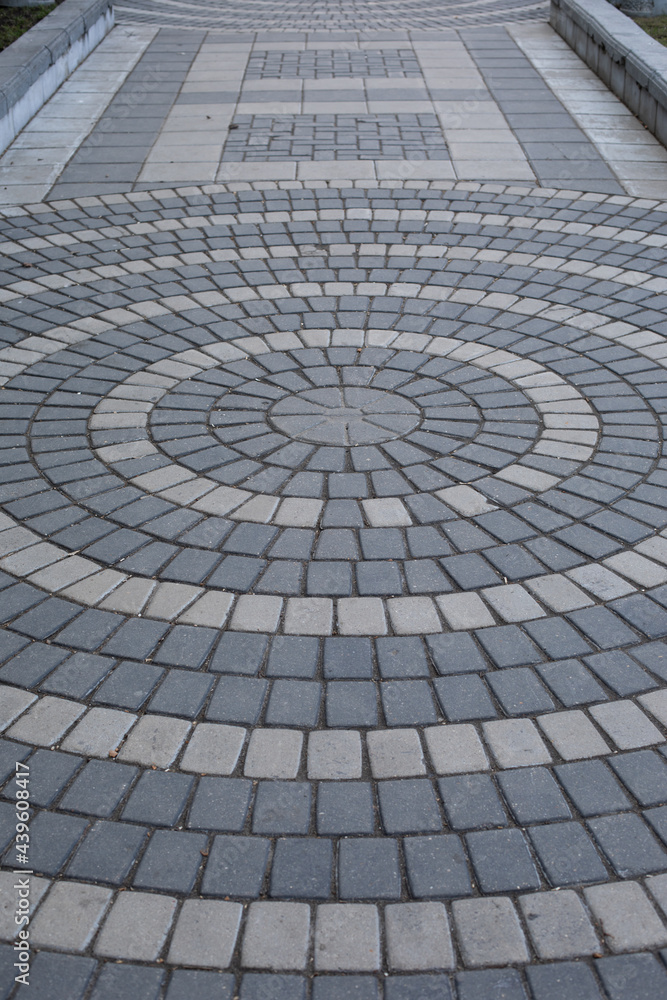 The path is paved with two shades of gray stone. Round pattern on a paved path in a park, vertical texture