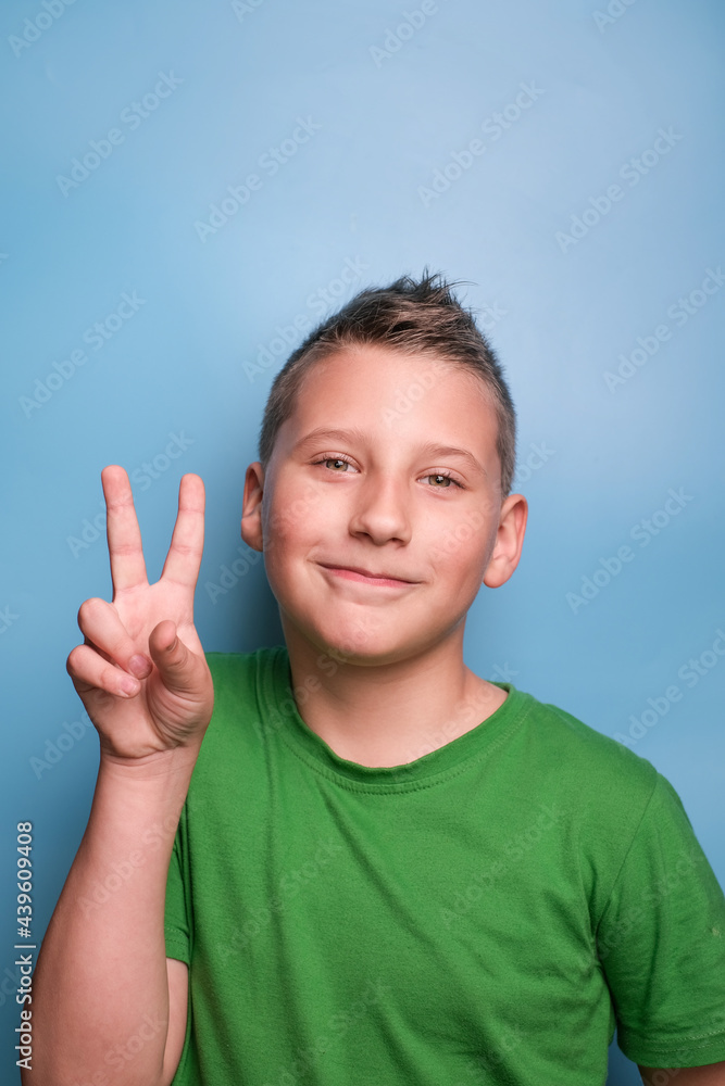 Head shot of emotional adorable boy showing viktory sign by hand. Portrait on blue background Head shot of emotional adorable boy showing viktory sign by hand. Portrait on blue background