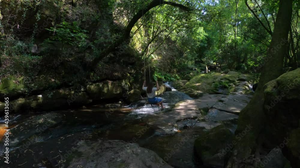 SLOW MOTION - Slightly moving empty rustic wooden swing hanging by rope on a tree branch over Sampaio river near the Ribeiro de Sampaio Leisure Park in Cinfaes, near the village of Mourilhe, Portugal.