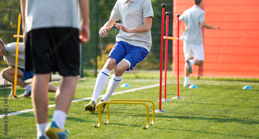 Obraz premium Teenage Football Players on Training Camp. Young Boys Running Slalom Track Between Training Poles and Jumping Over Hurdles. Soccer Training Equipment