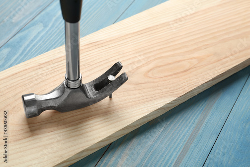 Hammer pulling metal nail out of plank on light blue table, closeup