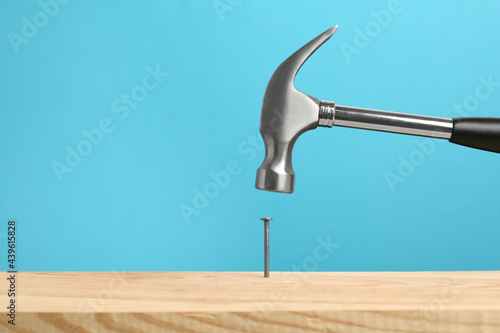 Fototapeta Hammering nail into wooden surface against light blue background