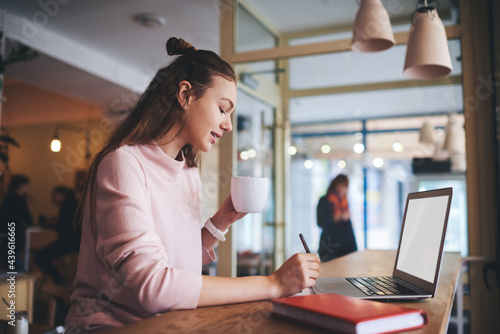 Young freelance taking notes in planner sitting at table in cafe