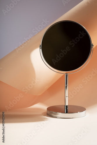 Silver cosmetic mirror on table. Copy space. Focus on shadows