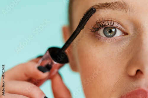 Photos Young blonde woman applying mascara and looking at camera