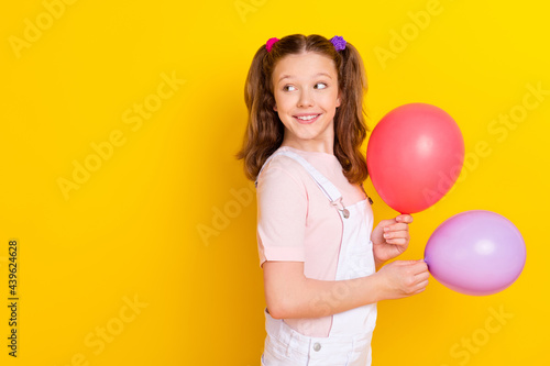 Photo portrait schoolgirl with tails keeping air balloons looking copyspace isolated vivid yellow color background © deagreez