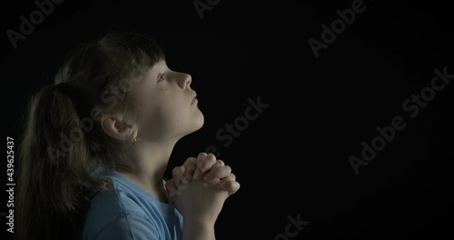 Child hope for God. A calm child puts her hands and pray on the black background. photo