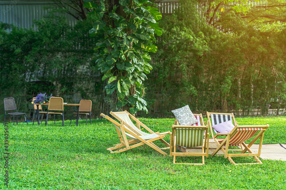 Many deck chairs and pillows with wooden table in the courtyard is surrounded by shady green grass. Comfortable pillows on outdoor patio chair and table in garden. Summer vacation. Selective focus. Many deck chairs and pillows with wooden table in the courtyard is surrounded by shady green grass. Comfortable pillows on outdoor patio chair and table in garden. Summer vacation. Selective focus.