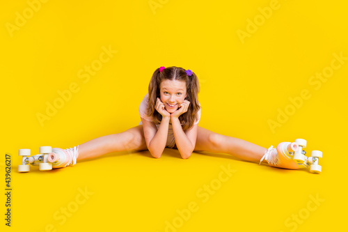 Full length body size photo schoolgirl wearing rollers doing stretching exercises isolated bright yellow color background