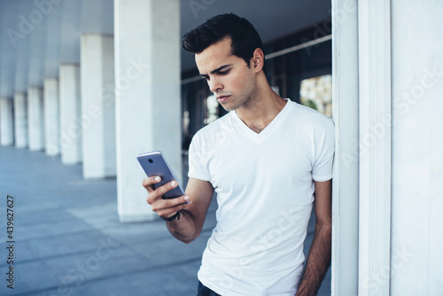 Young hipster guy in casual clothes connecting to wireless for chatting and messaging in social media networks, millennial man checking mobile sms writing text for sending via smartphone application