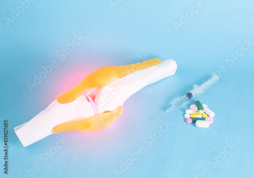 Knee joint mockup on a blue background and pills with a syringe. The concept of treatment of the knee joint with chondroprotectors and anti-inflammatory drugs. photo