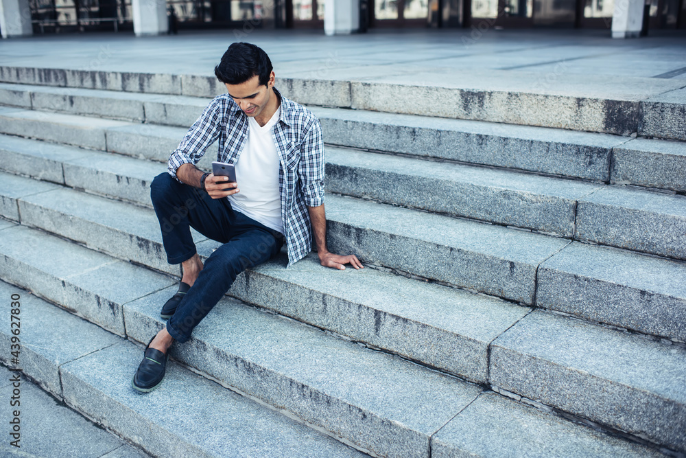 Millennial male tourist connecting to 4g wireless internet on cellular gadget for installing application, young hipster guy browsing media publication in social networks resting at urban setting Millennial male tourist connecting to 4g wireless internet on cellular gadget for installing application, young hipster guy browsing media publication in social networks resting at urban setting