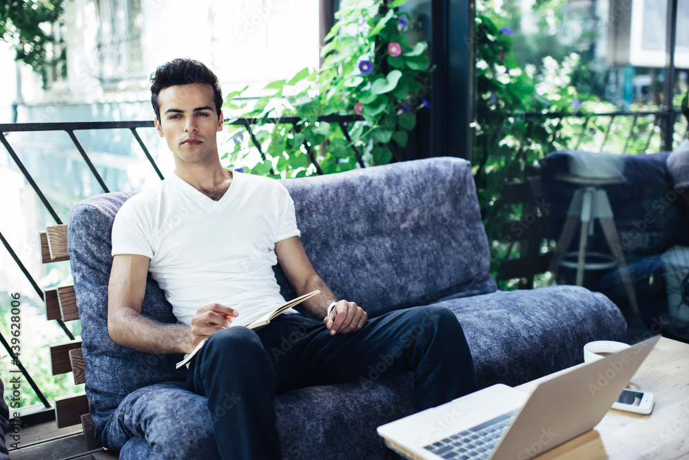 Portrait of male freelancer with education textbook and laptop computer for web e learning looking at camera, skilled student with notepad for organisation planning and digital netbook posing outdoors