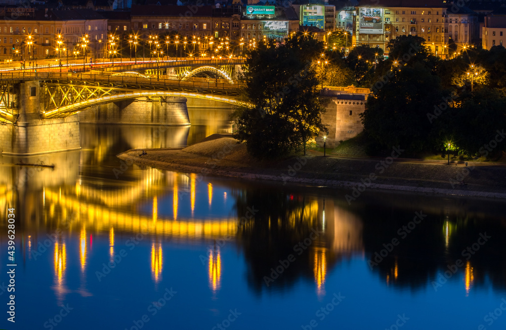 View of the bright yellow bridge illuminated at night in the blue hour, reflection in the blue painted water 