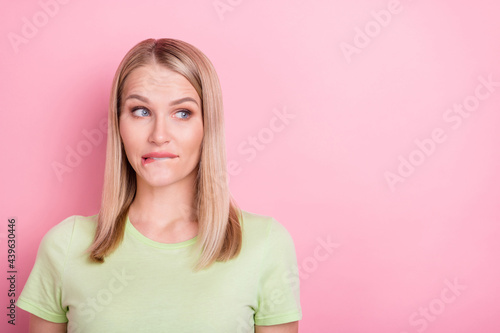 Photo of curious gossip lady tender bite lip look side empty space wear green t-shirt isolated on pink background